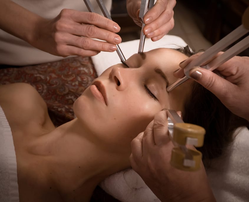 Beautiful woman relaxing at sound face massage session with tuning forks